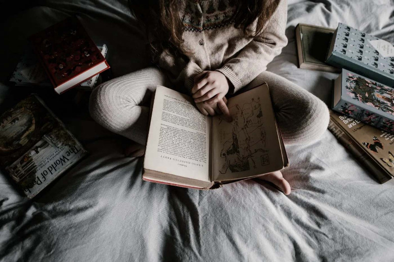 A female with multiple reading multiple books on her bed